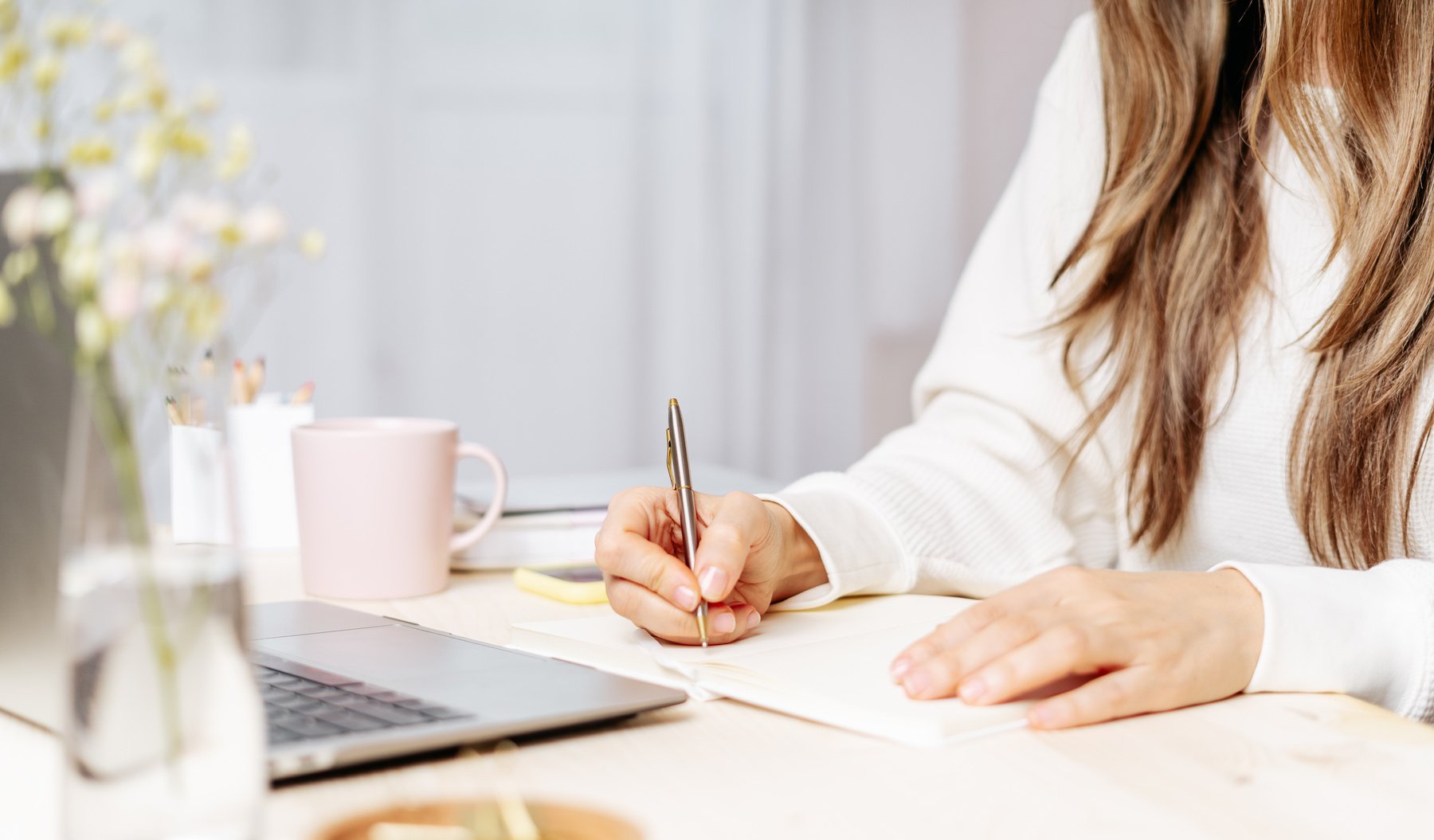 Woman writes in notebook on desk with laptop